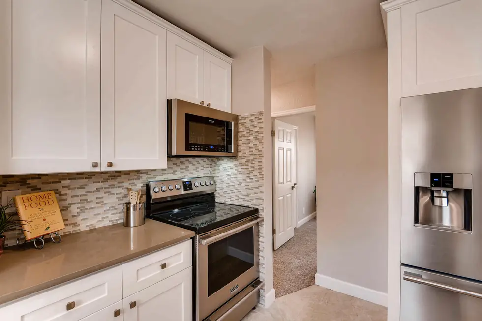 White shaker kitchen with a glass mosaic backsplash behind a stainless range
