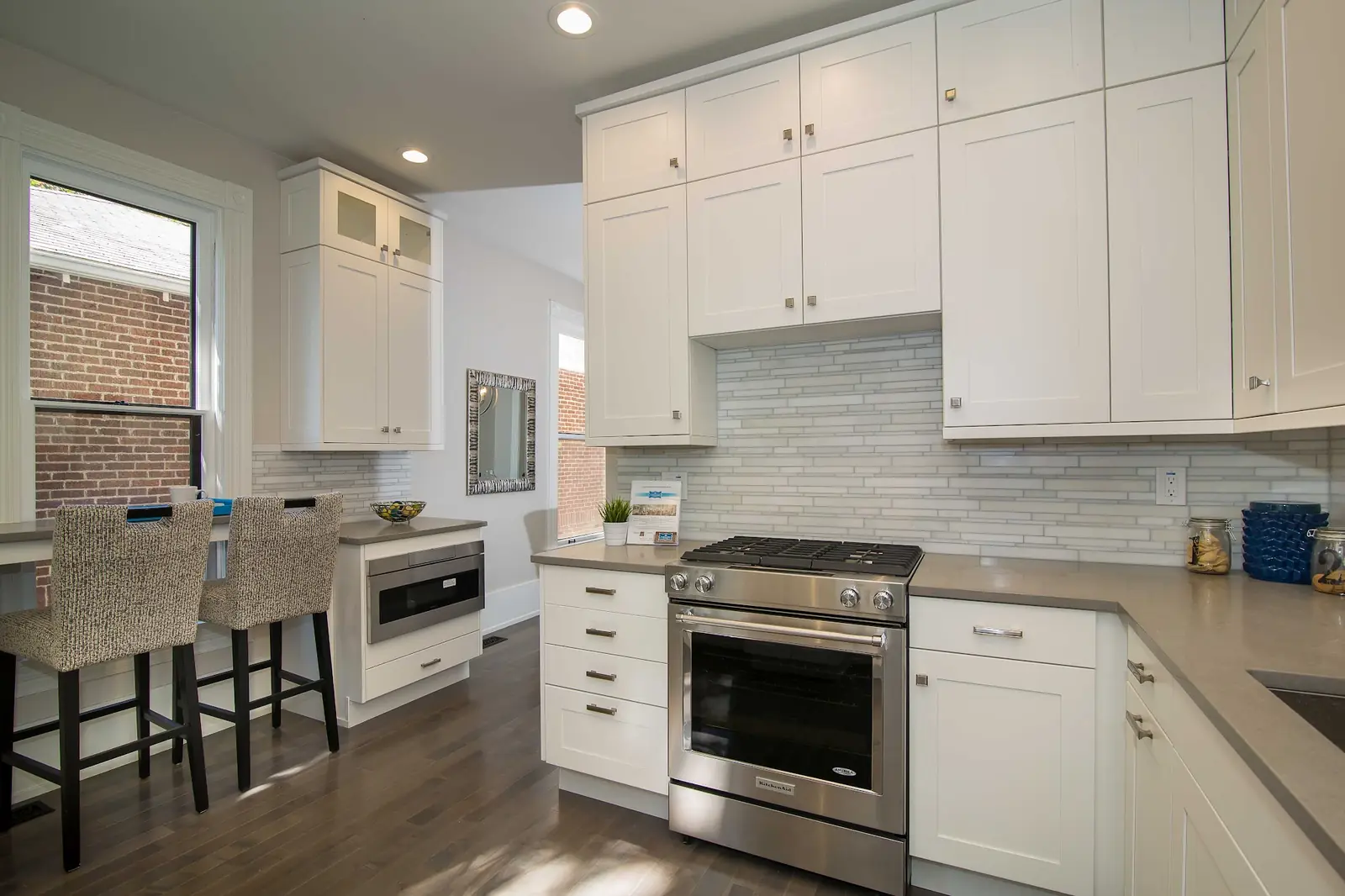 White shaker kitchen with a gas range, tall upper cabinets and a window onto brick